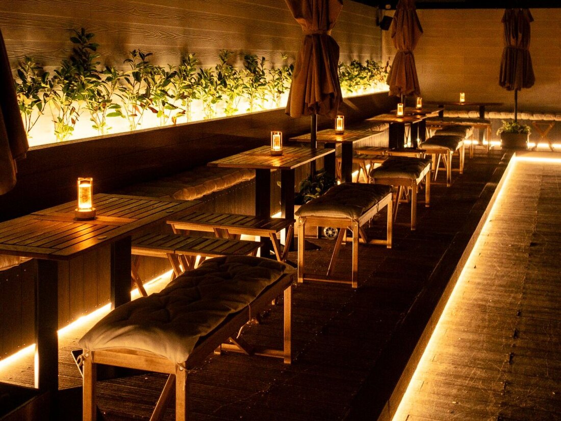 The La-Yam rooftop in the evening, with candlelit tables, cushioned benches and warmly illuminated planting.