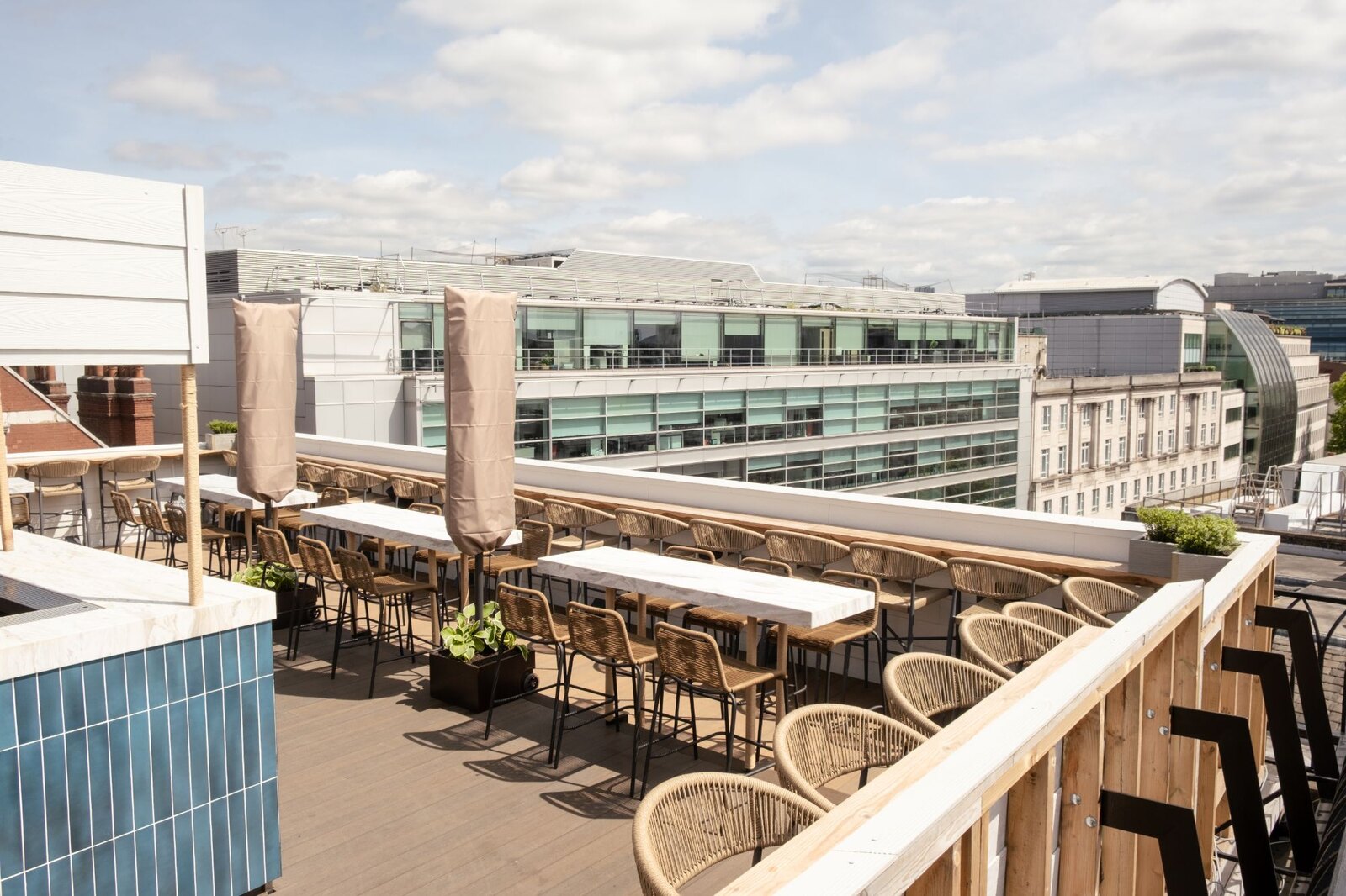 The La-Yam rooftop terrace above High Holborn in daylight, with marble bar tables, woven seating and the London skyline beyond.